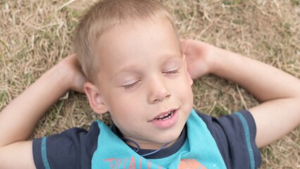 Little Happy and Child Boy Laying with closed eyes on Yellow Lawn Dry Grass Hay in Park. Summer Time, Nature, Dreams, Lifestyle Country life farm village. Smilling Face Close up Looking at Camera