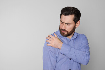 Man suffering from pain in his shoulder on light background, space for text. Arthritis symptoms