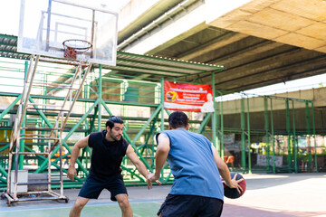 Fototapeta na wymiar Two man athlete playing streetball match shooting and defense basketball on outdoors court together in sunny day. Sportsman do sport training basketball at street court under highway in the city.