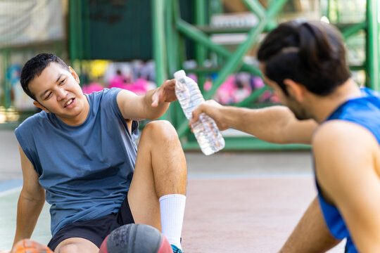 Two man friends athlete resting and drinking water together after play streetball on outdoors court in sunny day. Sportsman basketball player do sport training workout at street court in the city. - Powered by Adobe