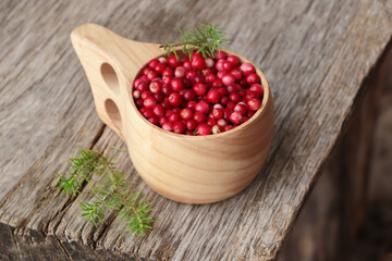 Cup with tasty ripe lingonberries and spruce twigs on wooden surface