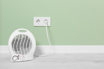 Electric fan heater near pale green wall indoors. Space for text