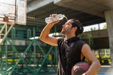 Caucasian sportsman basketball player drinking and pouring water from a bottle on his face after do...