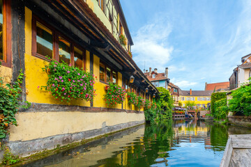 View of half timber homes and cafes from a boat on the Lauch canal in the historic medieval Petite Venice district of Colmar, France, in the Alsace region.	 - obrazy, fototapety, plakaty