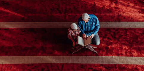 Muslim prayer father and son in mosque praying and reading holly book Quran together islamic education concept