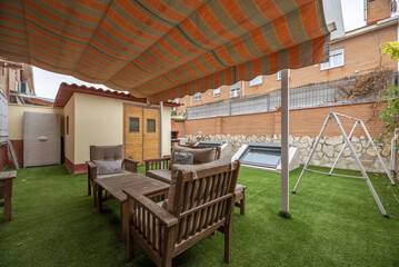 Backyard of a detached house with gazebo awning covering a set of teak table and chairs on a green...