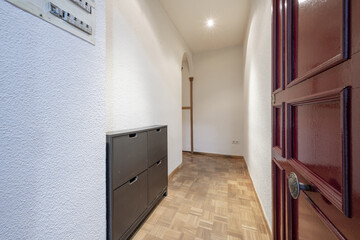 Entrance hall of a house with a red wood paneled door, a checkerboard parquet floor and an L-shaped hallway