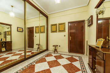 Entrance hall of a house with a three-section built-in wardrobe with sliding mirror doors with golden edges and a checkered stoneware floor with borders