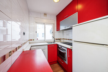 Kitchen with red cabinets, white countertops and multi-colored appliances with a white aluminum window