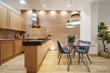 Apartment with open kitchen with wooden furniture with black marble countertop and glass and metal office table with blue velvet upholstered chairs