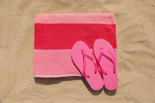 Beach towel with slippers on sand, top view