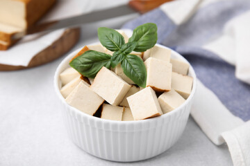 Bowl of smoked tofu cubes with basil on white table, closeup