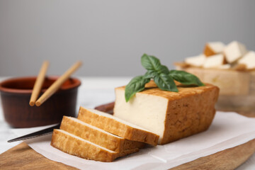 Board with smoked tofu, knife, basil and soy sauce on white wooden table