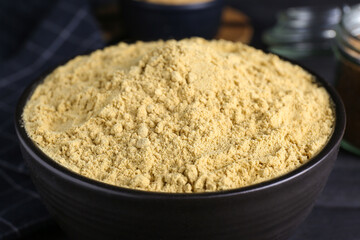 Bowl of aromatic mustard powder on black wooden table, closeup