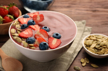 Bowl of delicious smoothie with fresh blueberries, strawberries and pumpkin seeds on wooden table