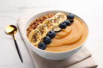 Delicious smoothie bowl with fresh blueberries, banana and granola on white table, closeup