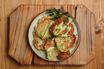 Tasty parsnip cutlets with sauce on wooden table, top view