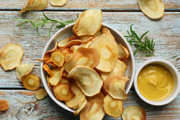 Tasty homemade parsnip chips with sauce and rosemary on old light blue wooden table, flat lay