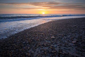 Sonnenuntergang am steinigen Strand mit Wellen und Sonne am Horizont