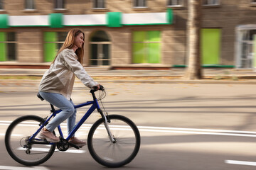 Happy beautiful woman riding bicycle in city, motion blur effect