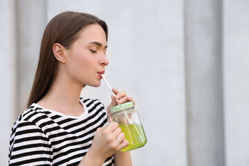 Young woman with mason jar of fresh juice outdoors, space for text