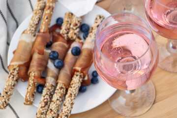 Glasses of delicious rose wine and food on white picnic blanket, closeup