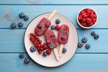 Plate of tasty berry ice pops on light blue wooden table, flat lay. Fruit popsicle © New Africa