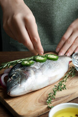 Woman sprinkling dorado fish with seasoning at wooden table, closeup