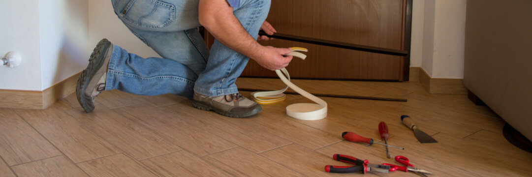 Image Of A Handyman Installing Seals And Door Sills To Improve The Thermal Insulation Of The House. Horizontal Banner 