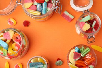 Fototapeta na wymiar Frame of tasty jelly candies in jars on orange background, flat lay. Space for text