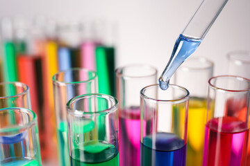 Dripping liquid from pipette into test tube on grey background, closeup