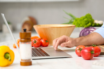 Man making dinner while watching online cooking course via laptop in kitchen, closeup