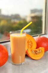 Tasty pumpkin juice in glass, whole and cut pumpkins on windowsill indoors