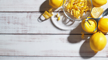 Bowl with peel pieces, fresh lemons and zester on white wooden table, flat lay. Space for text