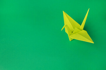 Paper origami crane on green background, space for text