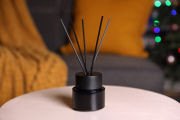 Aromatic reed air freshener on white wooden side table in cozy room