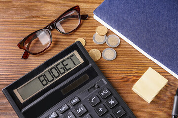 Budget plan. Calculator, glasses, coins and notebook on wooden table, above view