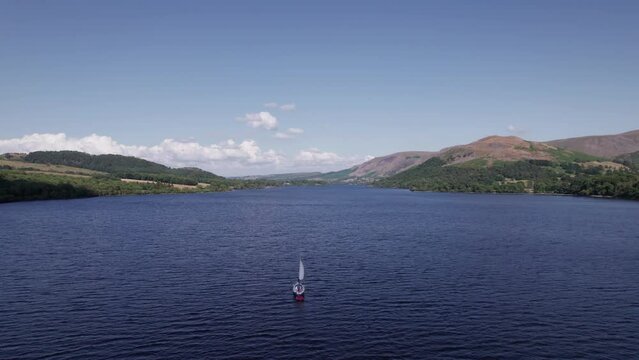 Slow drone shot flying forward over a sail boat on a sunny day, Ullswater, Lake District, Cumbria, UK