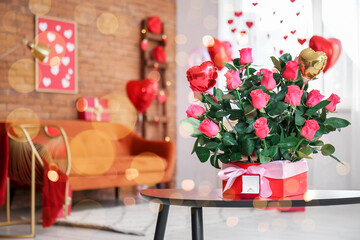 Box with beautiful rose flowers and engagement ring on table in living room decorated for Valentine's Day