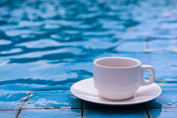 White cup of coffee by the edge of the pool, blue water background