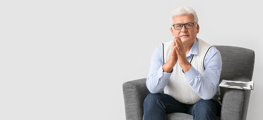 Male psychologist sitting in armchair on light background with space for text