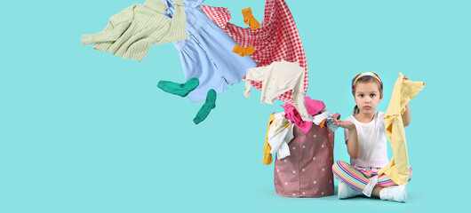 Obraz na płótnie Canvas Troubled little girl with flying dirty clothes and basket on blue background. Banner for design