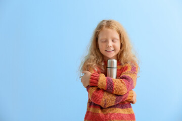 Little redhead girl with thermos on blue background
