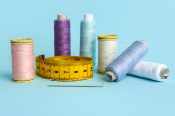 Thread spools, needles and measuring tape on color background
