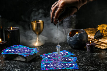 Fortune teller using pendulum and tarot cards to read future on dark background
