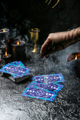 Fortune teller using pendulum and tarot cards to read future on dark background