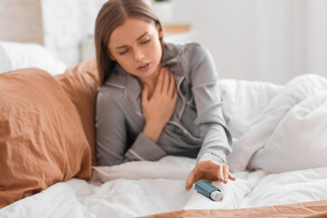 Sick young woman with inhaler in bed - obrazy, fototapety, plakaty