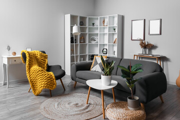 Interior of modern living room with black sofa, armchair and shelving unit