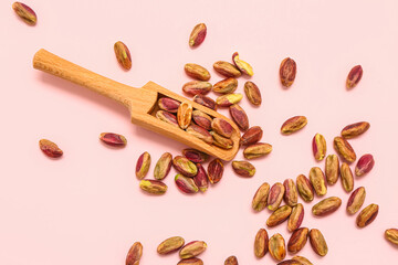 Tasty pistachio kernels and scoop on pink background