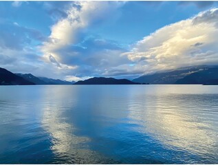 Obraz premium A sunny winter afternoon in Harrison Hot Springs, British Columbia, Canada. Blue sky, white cloudy, and beautiful reflection. Some waves and thin ice on the lake surface.